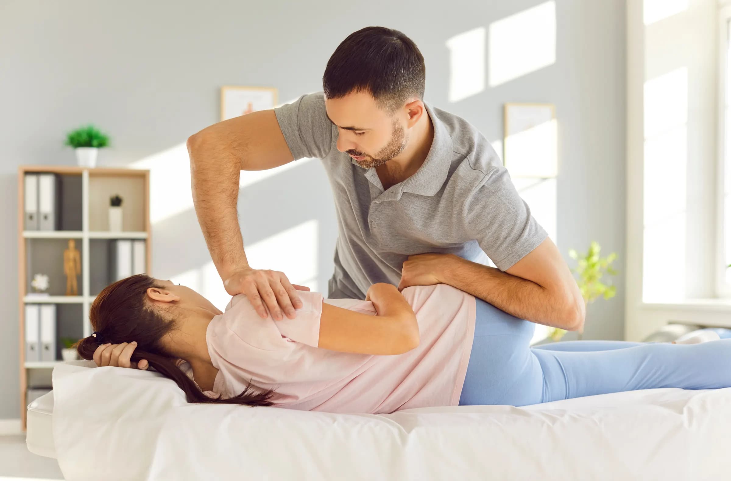 A physiotherapist treating a patient's back on a treatment couch in a bright clinic