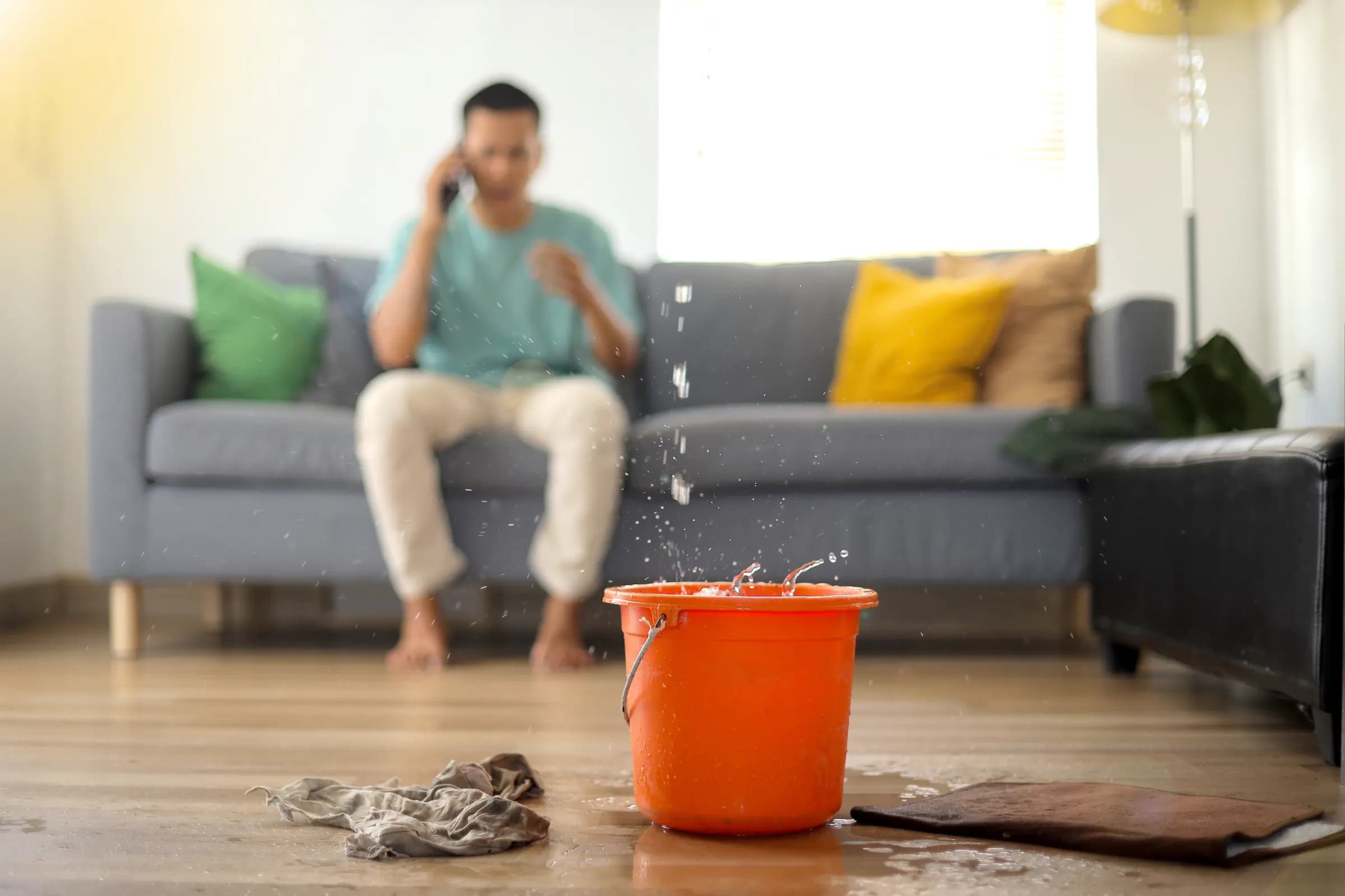 A tenant on the phone on his sofa while water drips from the ceiling into an orange bucket